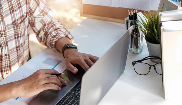 Close up of businessman or accountant hand holding pen working on laptop computer for calculate business data, accountancy document and calculator at office, business concept.