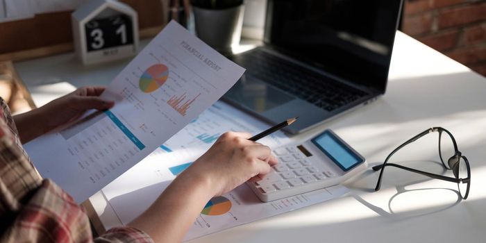 Close up of businessman or accountant hand holding pen working on calculator to calculate business data, accountancy document and laptop computer at office, business concept.