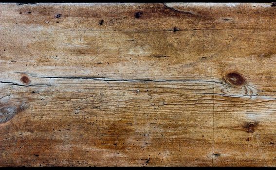 A horizontal rustic wooden board of aged wood. The wood is weathered, heavily textured and coloured yellow, gold and brown.