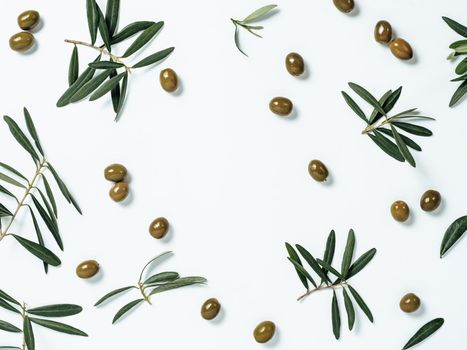 Pattern with green olives and olives tree leaves and branches on white background, copy space in center. Olive tree fruits and branches, top view or flat lay.