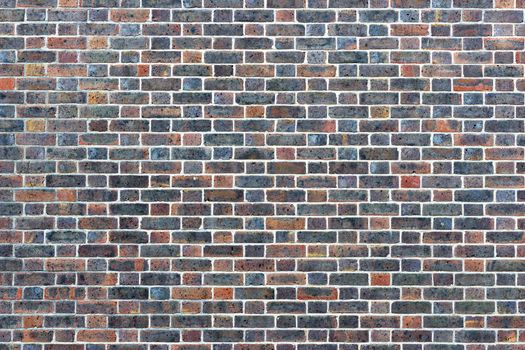 Photograph of a brick wall pattern. The bricks are red, blue, pink and purple in colour with white mortar.