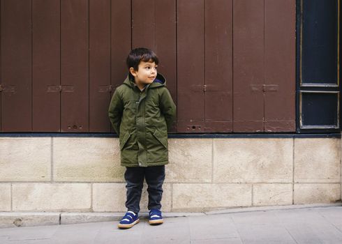 Little boy in green coat against vintage looking wall