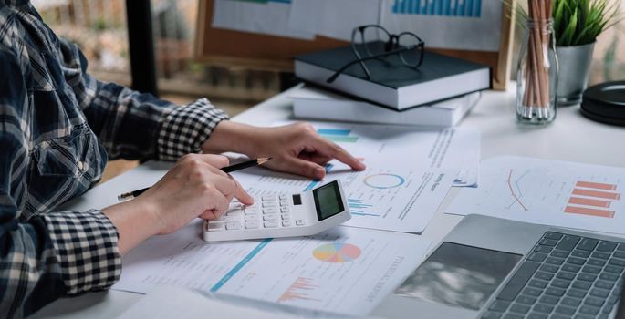 Bookkeeper or Businesswoman using a calculator to calculate report profit, analyzer graph balance, tax on table. Business Financial Concept