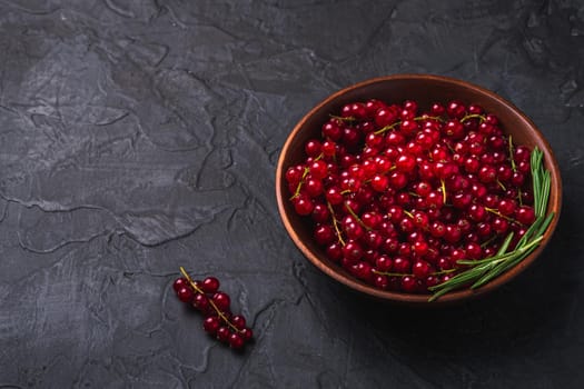 Fresh sweet red currant berries with rosemary leaves in wooden bowl, dark textured background, angle view copy space