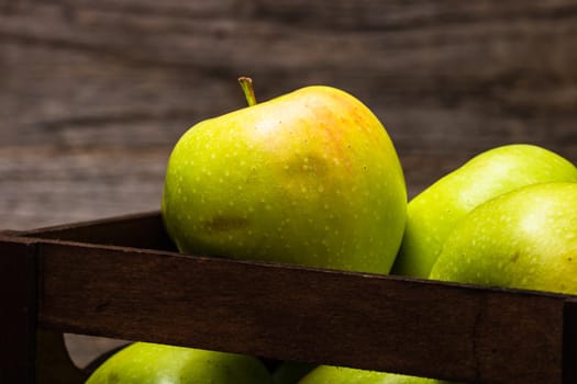 Wooden crate with ripe green apples on wooden table.