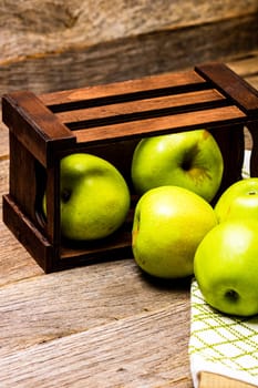 Wooden crate with ripe green apples on wooden table.