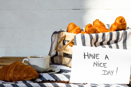 Coffee cup and buttered fresh French croissant on wooden crate. Food and breakfast concept. Morning message “have a nice day” on white board