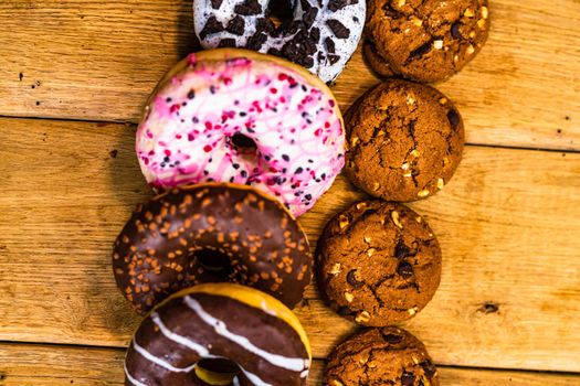 Colorful donuts on wooden table. Sweet icing sugar food with glazed sprinkles, doughnut with chocolate frosting. Top view with copy space