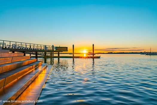 Sunrise over blue water of Tauranga harbour with intense golden glow on horizon with harbour steps and jumping platform.