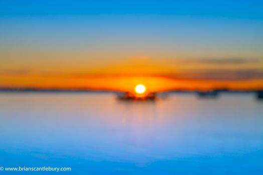 Abstract deliberate defocus coastal background for travel or coastal effects use sunrise over blue water of Tauranga harbour with intense golden glow on horizon.
