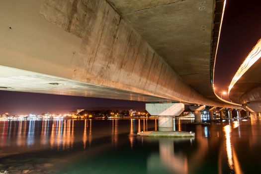 Under Tauranga Harbour Bridge at night with city lights across harbour.