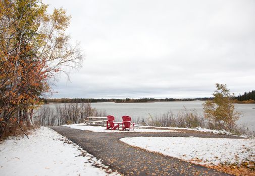 at Astotin Lake in Alberta, two red adirondack chairs celebrating Canada's 150th sit at the end of a path and overlook a lake in winter