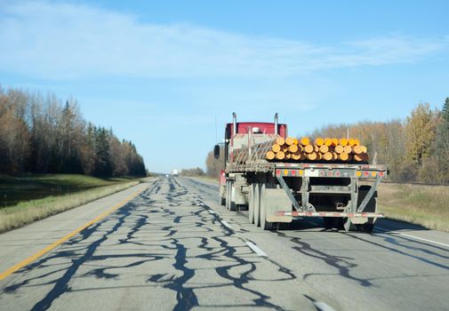 a transfer or 18 wheeler carrying pipes on a highway in blue sky 