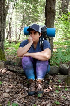 A woman sits on a rock looking puzzled or lost while hiking in the woods 