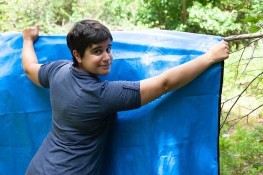 woman with a blue tarp hanging it on a tree branch outside 