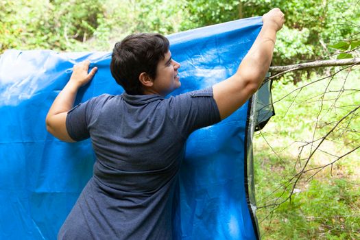 assembling a blue tarp in the forest to dry or cover 