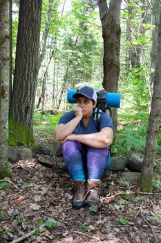 A hiker has become lost or anxious while hiking in the woods with a backpack and camping roll 