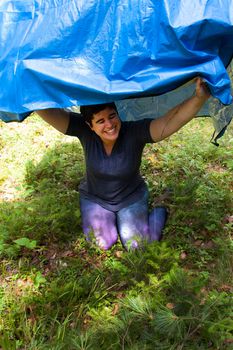 person hiding under a blue tarp in the woods giggling 