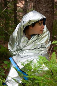  person looks around, frightened, while lost in the woods wearing a silver blanket 