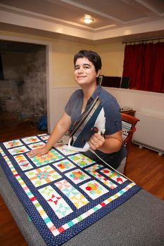 person smiles while holding a steaming iron and flattening a blanket on the ironing board 