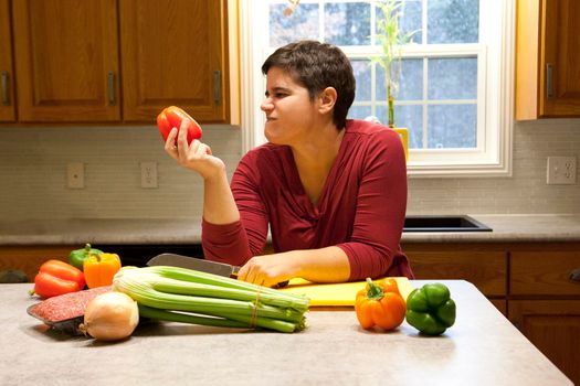 A woman holds a red bell pepper in her kitchen and makes an unhappy face