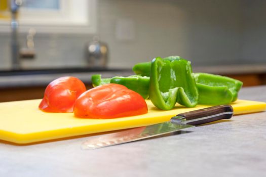 Green and red peppers on a cutting board with a knife 