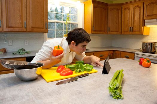 Chef in the kitchen holds a bell pepper and double checks ingredients or instructions on their tablet