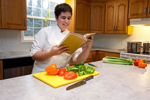 Woman in a chef's outfit in their kitchen with cut peppers smiles as they decide on a recipe