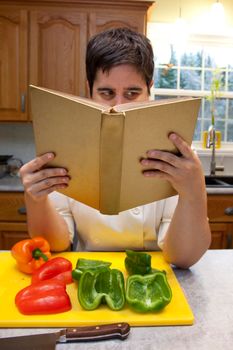  Person in chef's outfit holds a cookbook and reads instructions, with cut peppers in foreground