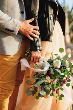 Groom holds bride's hand with a bouquet of flowers. Close-up of hands. High quality photo