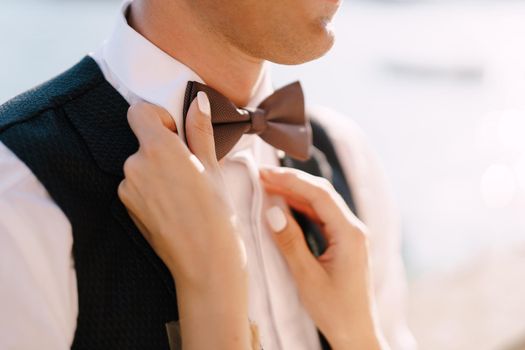 Close-up of the bride's hands. Plays with his fingers with the groom's bow tie.