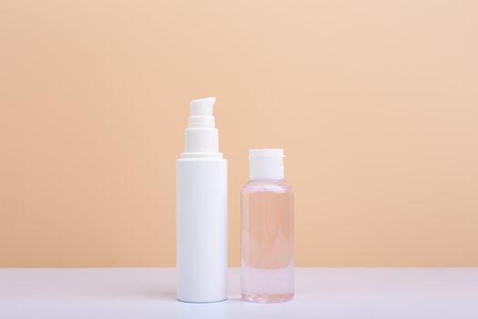 Face cream in white tube and skin lotion in transparent bottle against light beige background with copy space. Concept of beauty products and cosmetics with natural organic ingredients