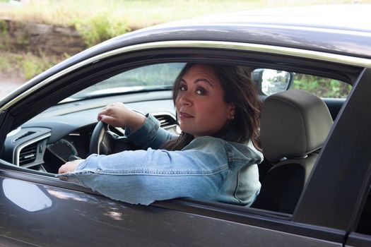 gorgeous hispanic woman in a jean jacket driving her sporty vehicle and looking chill