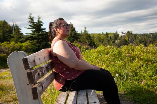 A woman sitting on a park bench beside grass blowing in the breeze on the east coast ocean