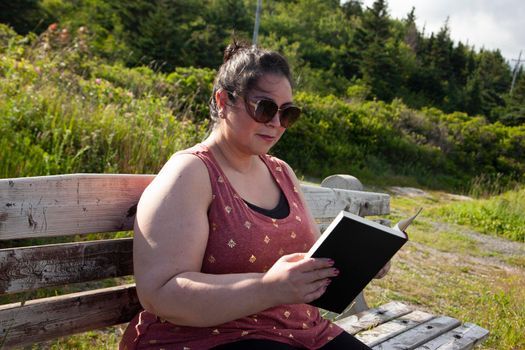 person on a park bench in the summer sun enjoying a good book 