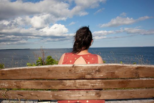 Looking over the shoulder of a person sitting on a park bench by the sea on a beautiful sunny day