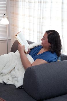 Woman comfortable and happy at home with a soft blanket and a good book 