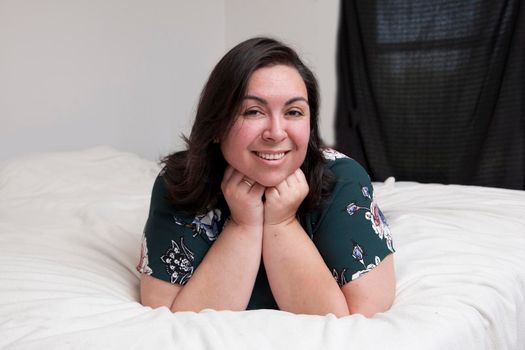 A relaxed happy woman lays on her bed at home looking at the camera in a portrait