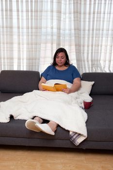 Person at home under a blanket reading a good hardcover novel