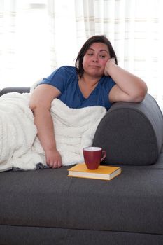 Woman sitting on her couch having finished her book and drink and is now bored and alone 