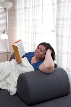 Happy hispanic woman is reading a book on her sofa, smiling and content 
