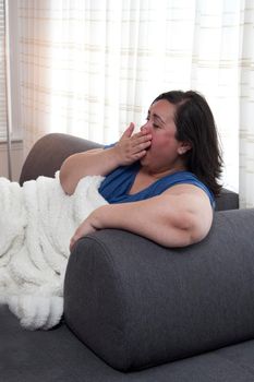 Woman is sleepy or bored, yawning on the sofa at home 