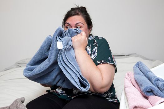 Woman with cheeky grin smells her freshly folded towels in her room