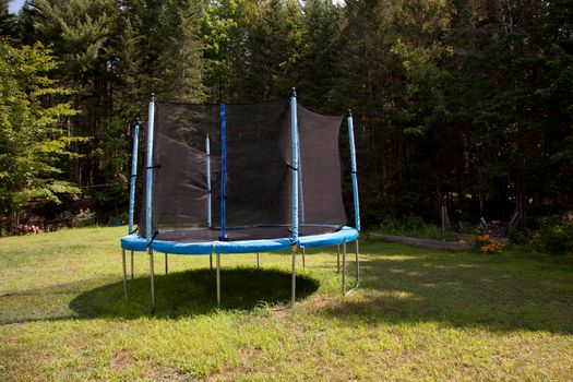 In someone's backyard a blue and black trampoline with netting to protect kids while jumping 