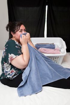 Latina woman on her bed folding towels and holding one close to her face