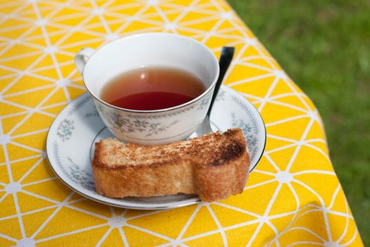 Snack and drink outside with teacup, spoon, saucer and toast on a yellow tablecloth