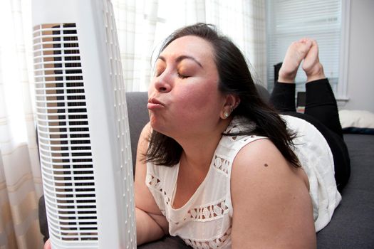 Woman kisses the cold breeze blowing in her face from her at home fan