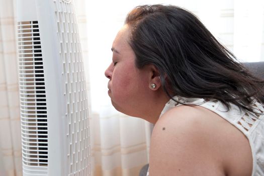 Woman enjoys the cool breeze of a fan at home in the heat