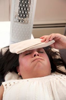 Woman lays in front of the fan with an ice pack on her forehead on a swealtering day 