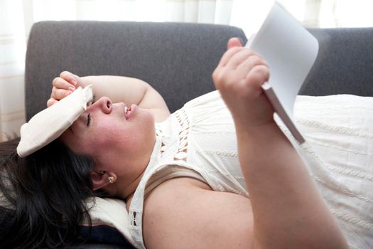 In a summer heatwave a woman has a cool pack on her head and uses a pad of paper to fan herself